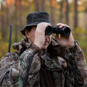 Get Ready for Deer Hunting This October: photo of hunter in camouflage holding up binoculars.